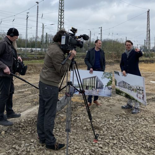 Kameramann und Toningeniur beim Interview mit Peter Bekaert und Thomas Hissel auf dem Baufeld des geplanten Neubaus in Düren. Beide halten Schilder vom Neubau in der Hand.